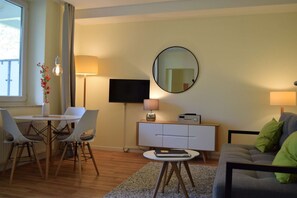 A modern living room with a dining area, a flat-screen TV, a round mirror, and a sofa with green cushions. - Close to the beach, balcony, free AHOI adventure pool - Strandresidenz Brandenburg FeWo 07 (Göhren)