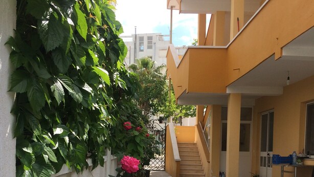 Un edificio con fachada amarilla, planta baja de concreto y una escalera que lleva a un nivel superior.