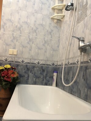 Un bagno con lavandino bianco, doccia con soffione manuale e rubinetto a muro.