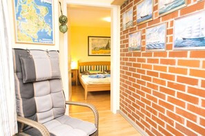 Ein Zimmer mit einem Korbstuhl, einem Bett, einer Karte an der Wand und gerahmten Meeresbildern.