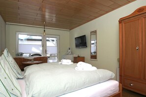 Ein Schlafzimmer mit einem Bett, einem Holzschrank, einem Fernseher, einem Fenster mit Jalousien und einem Deckenventilator.