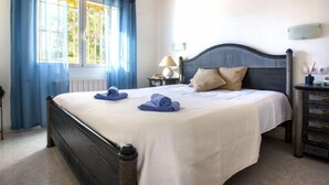 Quarto com cama, mesa de cabeceira, abajur e janela com cortinas.