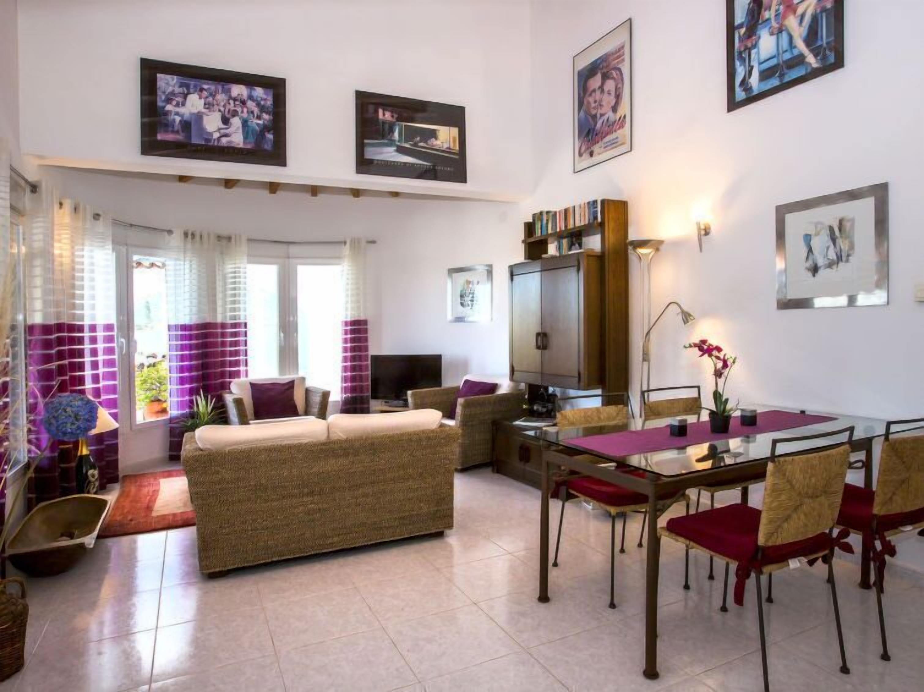 Una sala de estar con sofá, televisión, mesa de comedor con sillas y estantería.
