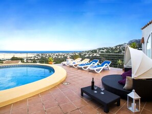 Un espace piscine sur le toit offrant une vue sur la mer et les collines, avec des chaises longues, une petite table avec une bouteille et des verres, et un coin salon abrité.