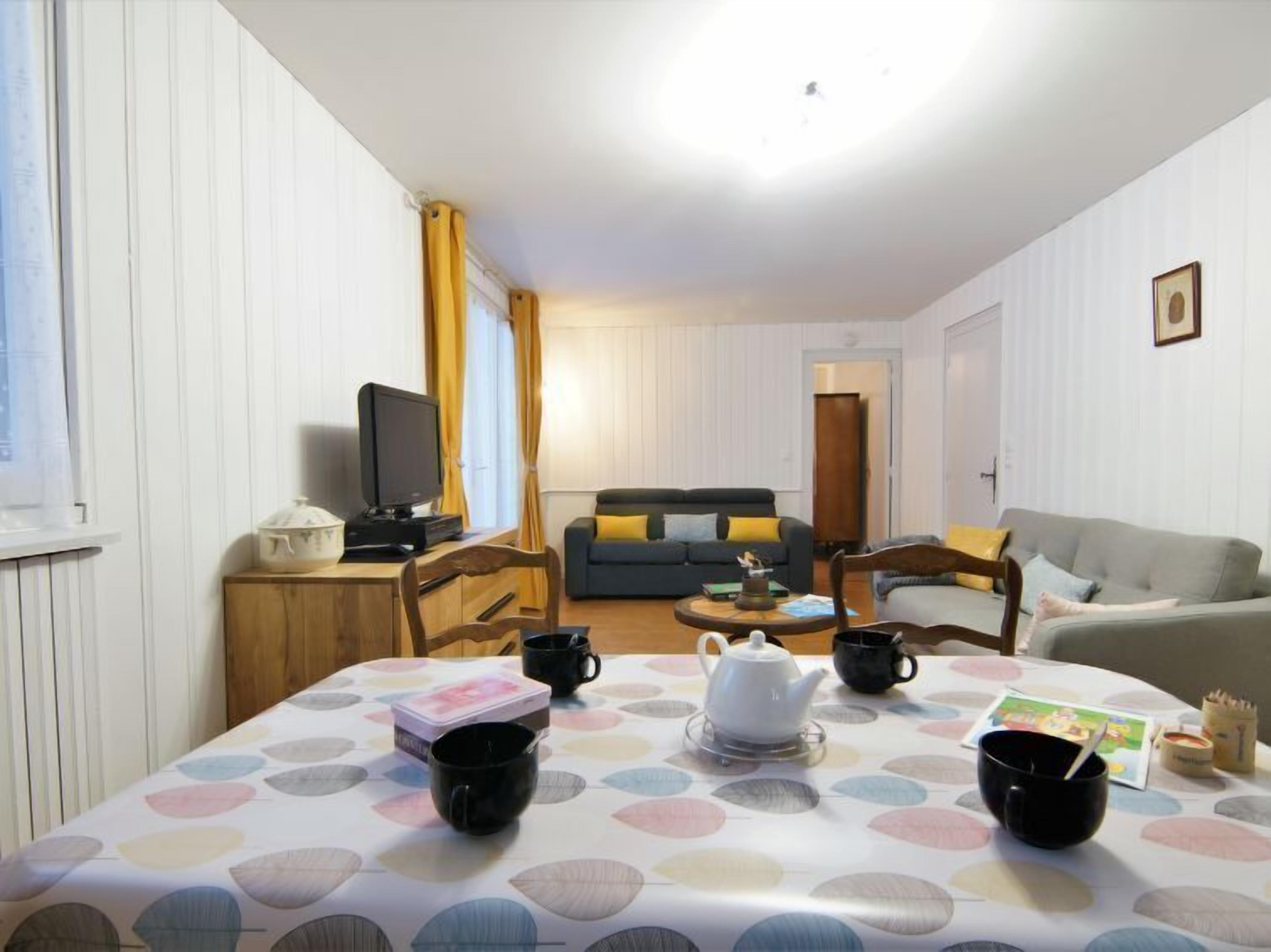 Un salon chaleureux avec un canapé, un téléviseur et une table à manger mise avec des tasses et une théière.