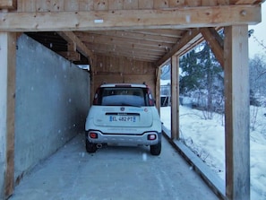 A white car parked inside a wooden structure with a snowy outdoor scene visible through the open sides.