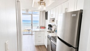 Een keuken met een roestvrijstalen koelkast, witte kasten, een eethoek met uitzicht op zee en een plafondventilator.