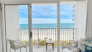 Een balkon met uitzicht op de oceaan, witte meubels en een houten vloer.