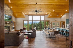 A spacious living area with a fireplace, a large window offering a mountain view, and a kitchen area with bar stools.