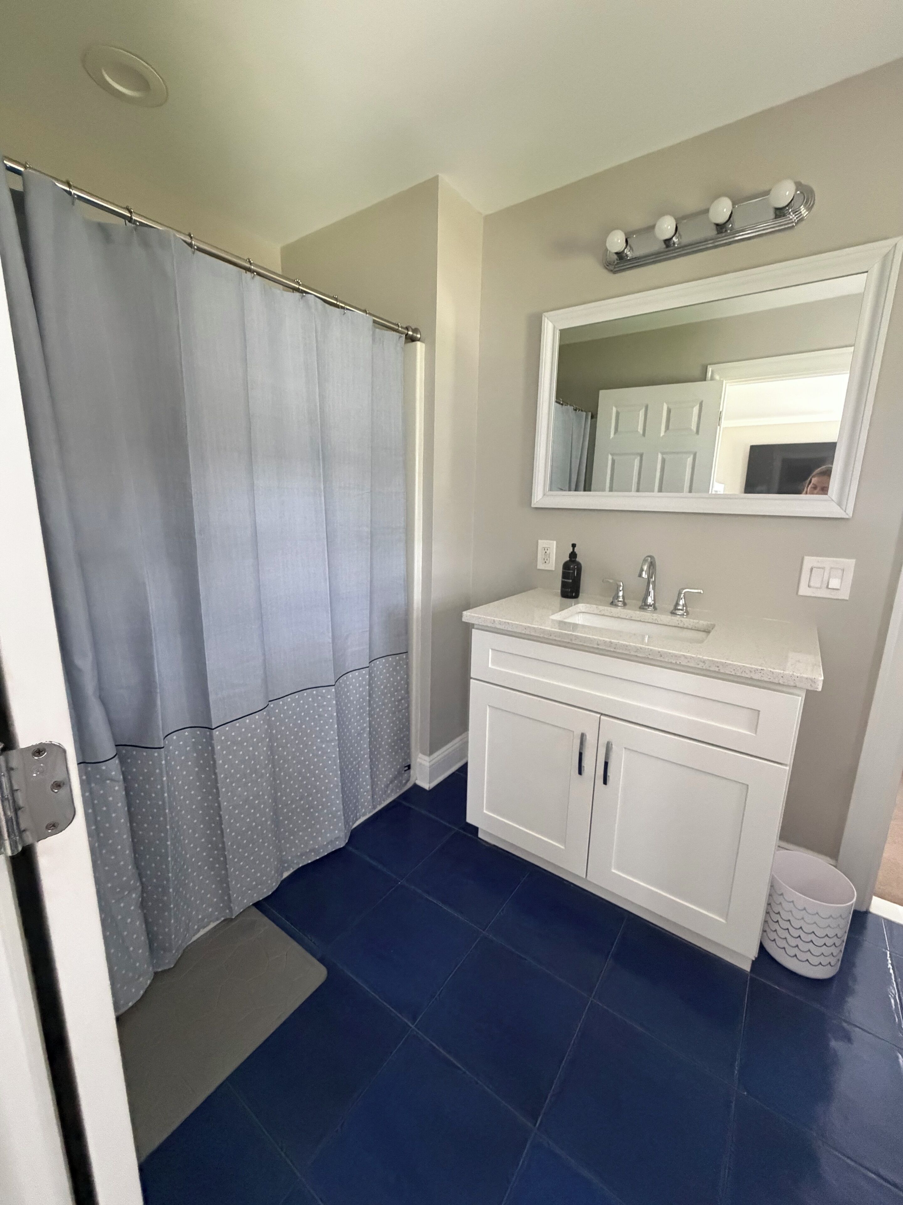 Une salle de bain avec un rideau de douche, un lavabo avec un miroir et une poubelle.