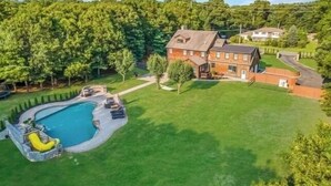 Uma casa grande com piscina, rodeada por um gramado bem cuidado e árvores.