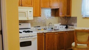 Una cocina con armarios de madera, estufa, microondas y un comedor con una silla y una mesa.
