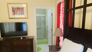 Habitación de hotel con una cama, un televisor sobre una cómoda, una puerta que da a un baño y una cortina estampada.