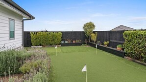 Un jardin avec une pelouse artificielle, trois drapeaux blancs et diverses plantes.