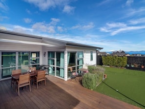 A modern house with a wooden deck, a glass-enclosed patio, and a well-maintained lawn.