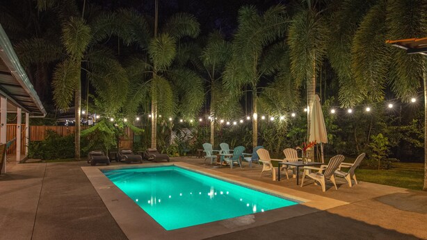 Uma piscina com um deck revestido, rodeada por espreguiçadeiras e uma fileira de luzes.