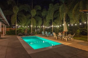 Ein Schwimmbecken mit gefliestem Sonnendeck, umgeben von Liegestühlen und einer Lichterkette.
