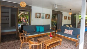 Uma ampla área externa com assentos de madeira e um sofá azul, com uma pequena mesa e uma planta decorativa.