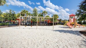 Ein Spielplatz mit Schaukeln und Rutschen, umgeben von Palmen und Bänken.
