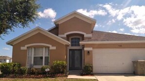A two-story house with a front garage, a small porch, and a well-maintained lawn. - Entire house w/ heated  pool-10 minutes from Disney parks. (Kissimmee)
