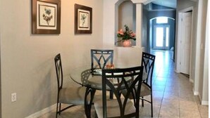 A dining area with a round table and four chairs, framed pictures on the wall, and a vase with flowers on a shelf. - Entire house w/ heated  pool-10 minutes from Disney parks. (Kissimmee)