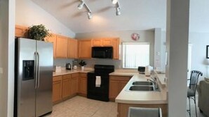 A modern kitchen with stainless steel appliances, wooden cabinets, and a central island. - Entire house w/ heated  pool-10 minutes from Disney parks. (Kissimmee)