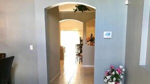 A hallway with a tiled floor, a dining area with chairs and a table, and a potted plant with flowers. - Entire house w/ heated  pool-10 minutes from Disney parks. (Kissimmee)