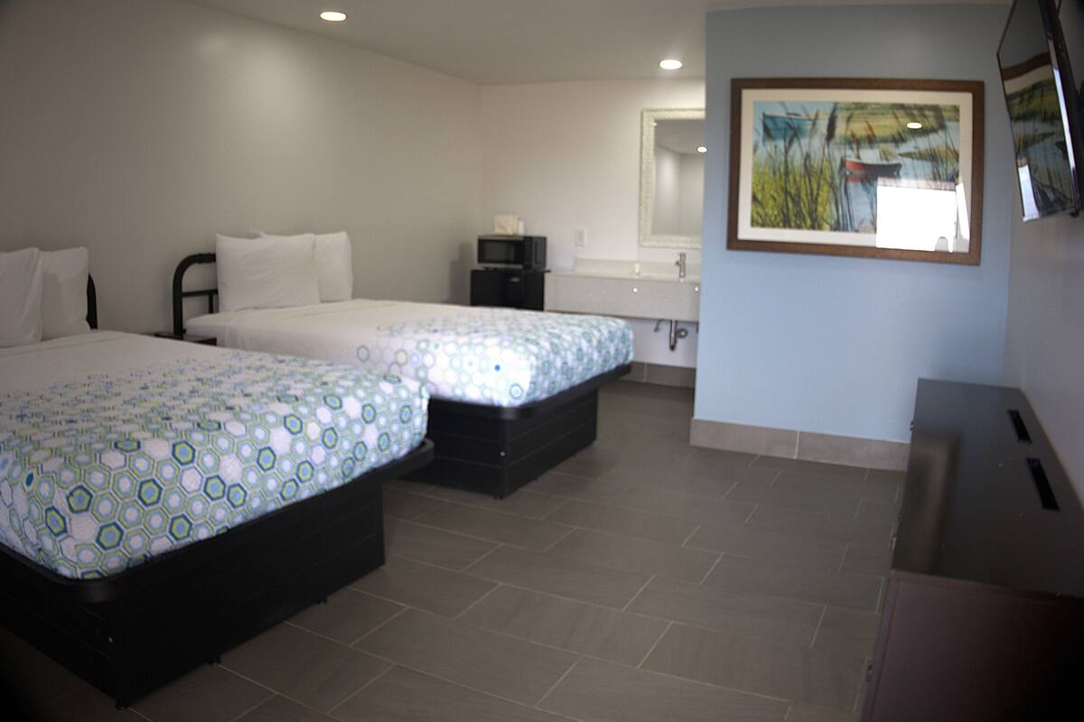 A hotel room with two beds, a small desk, a mirror, and a painting on the wall.