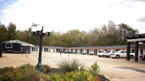 A motel with a parking lot, a covered outdoor seating area, and a decorative street lamp. - Rodeway Inn (Livingston)