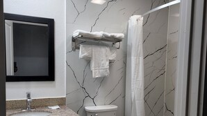 A bathroom with a marble-patterned wall, a toilet, a sink, a mirror, and a shower curtain. - Rodeway Inn (Livingston)