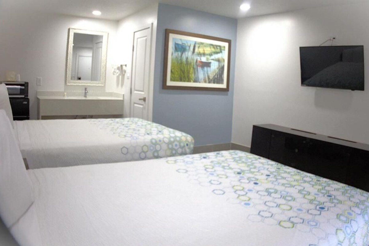 A hotel room with two beds, a bathroom, a TV, and a painting on the wall.