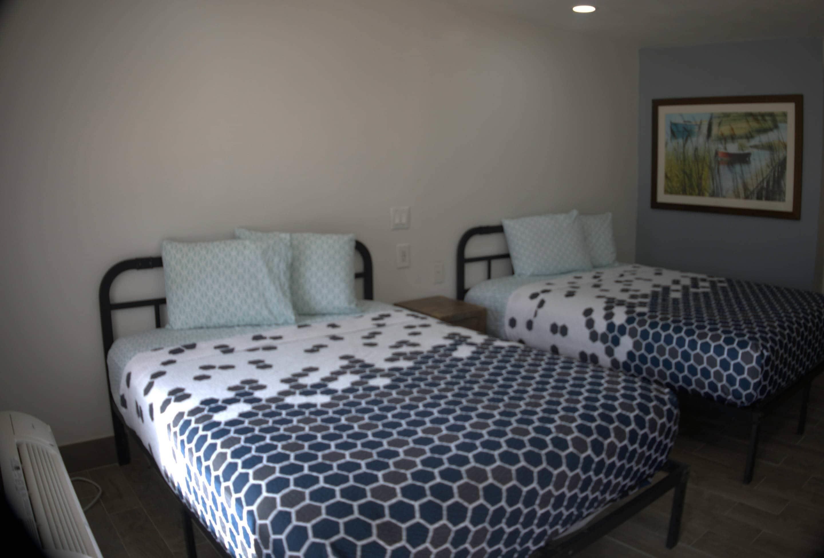 Two twin beds with patterned bedding, a radiator, and a painting on the wall.