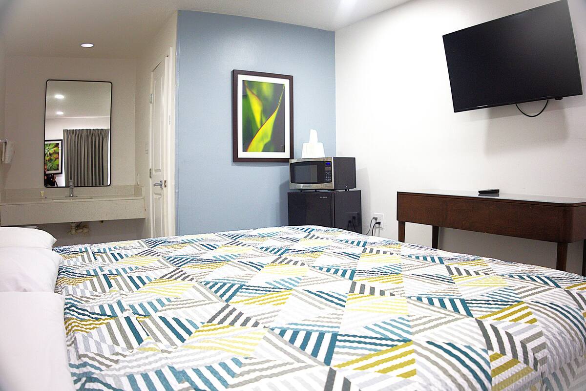 A hotel room with a bed, a TV mounted on the wall, a microwave, and a framed picture on the wall.