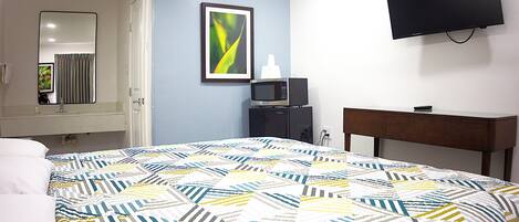 A hotel room with a bed, a TV mounted on the wall, a microwave, and a framed picture on the wall.