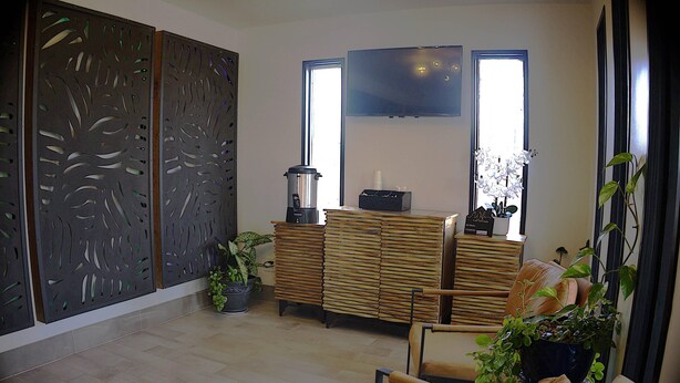 A modern living room with a wooden cabinet, a television mounted on the wall, and a large window providing natural light. - Rodeway Inn (Livingston)