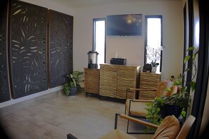 A modern living room with a wooden cabinet, a television mounted on the wall, and a large window providing natural light.