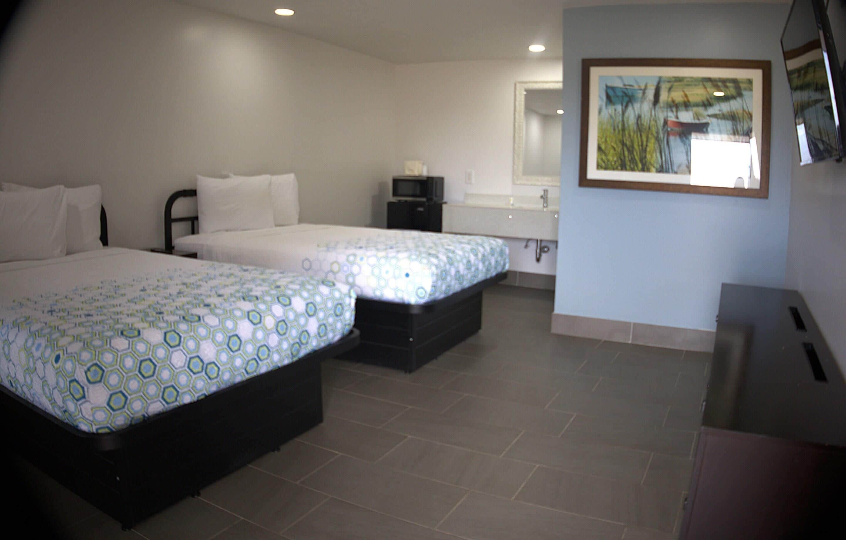 A hotel room with two beds, a small desk, a mirror, and a painting on the wall.