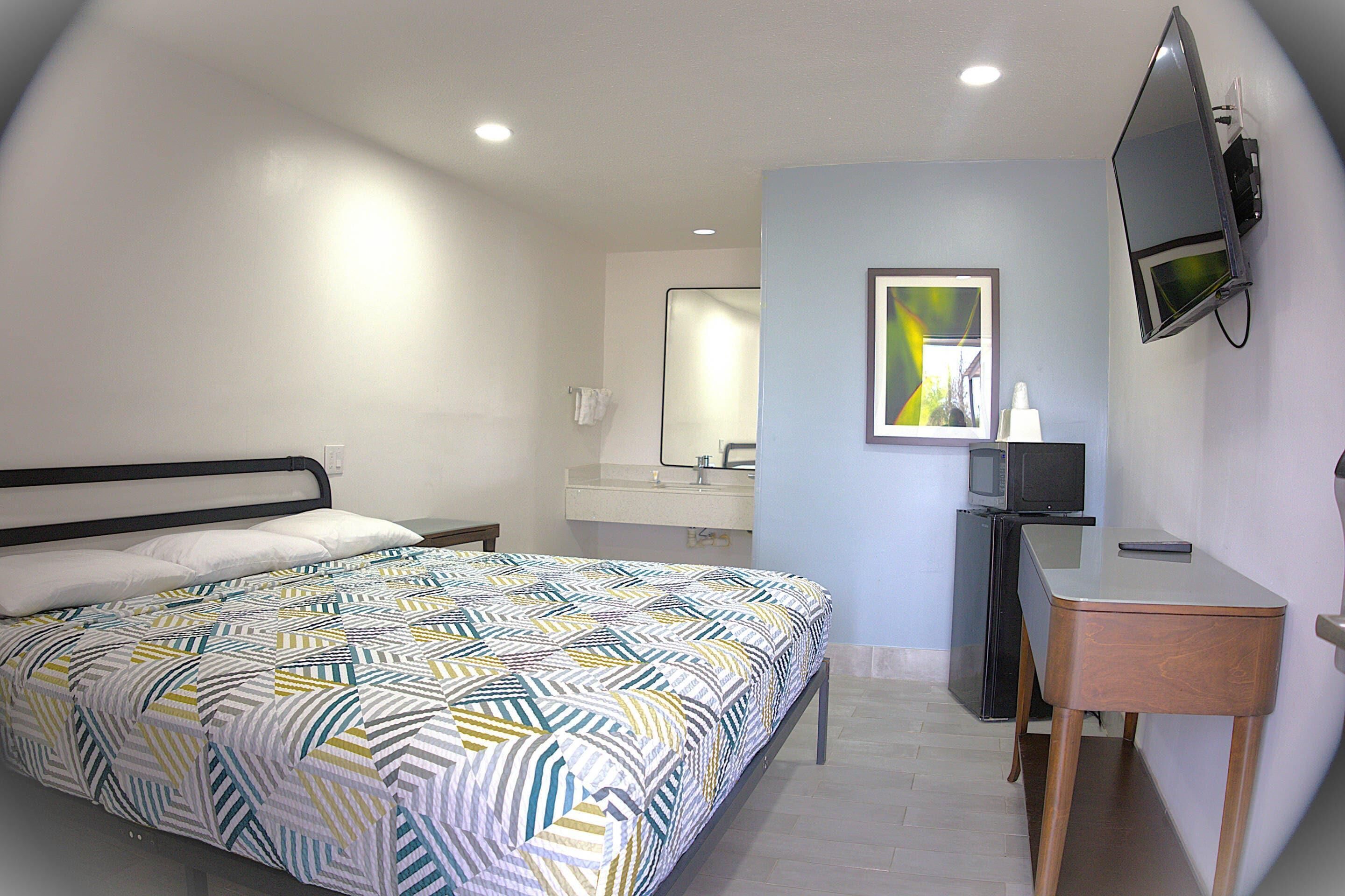 Un dormitorio con cama, escritorio, espejo y televisor.