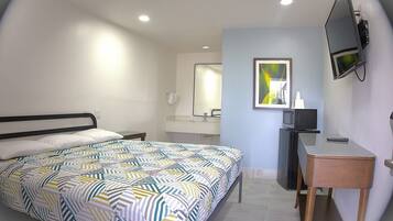 Un dormitorio con cama, escritorio, espejo y televisor.