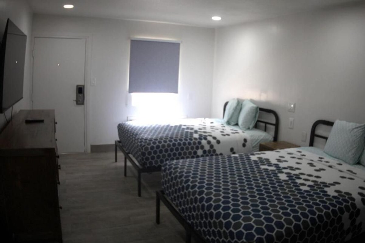 Un dormitorio con dos camas, un tocador, un televisor y una ventana con persianas.