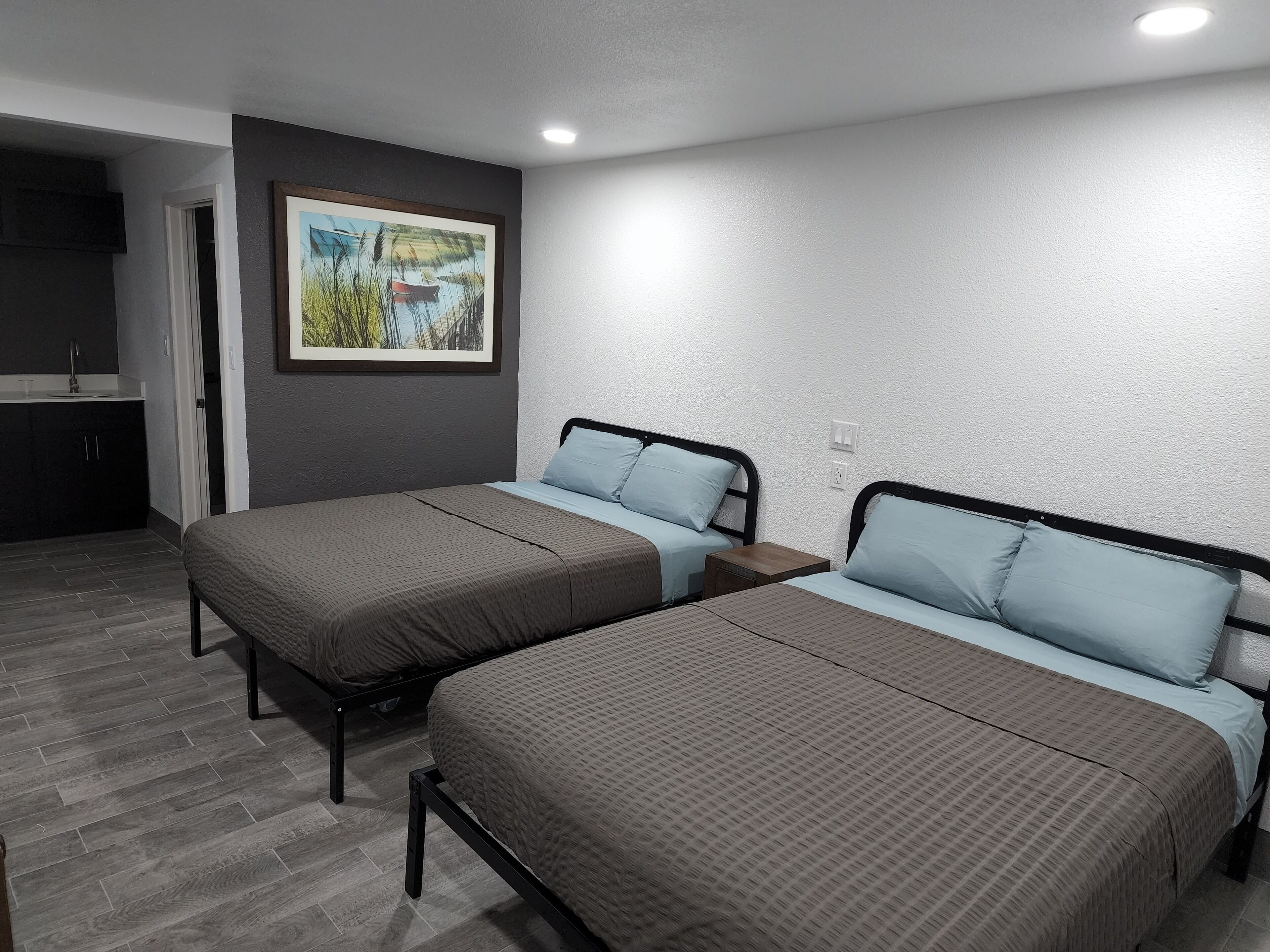 Ein Zimmer mit zwei Betten, einem kleinen Tisch, einem Bild an der Wand und einer Küchenzeile.
