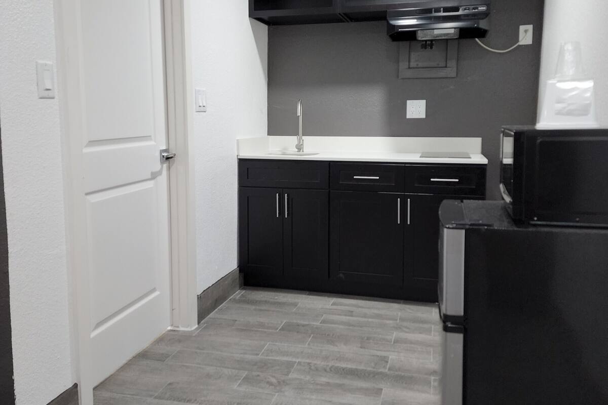 A compact kitchen with dark cabinets, a white countertop, and a black refrigerator.