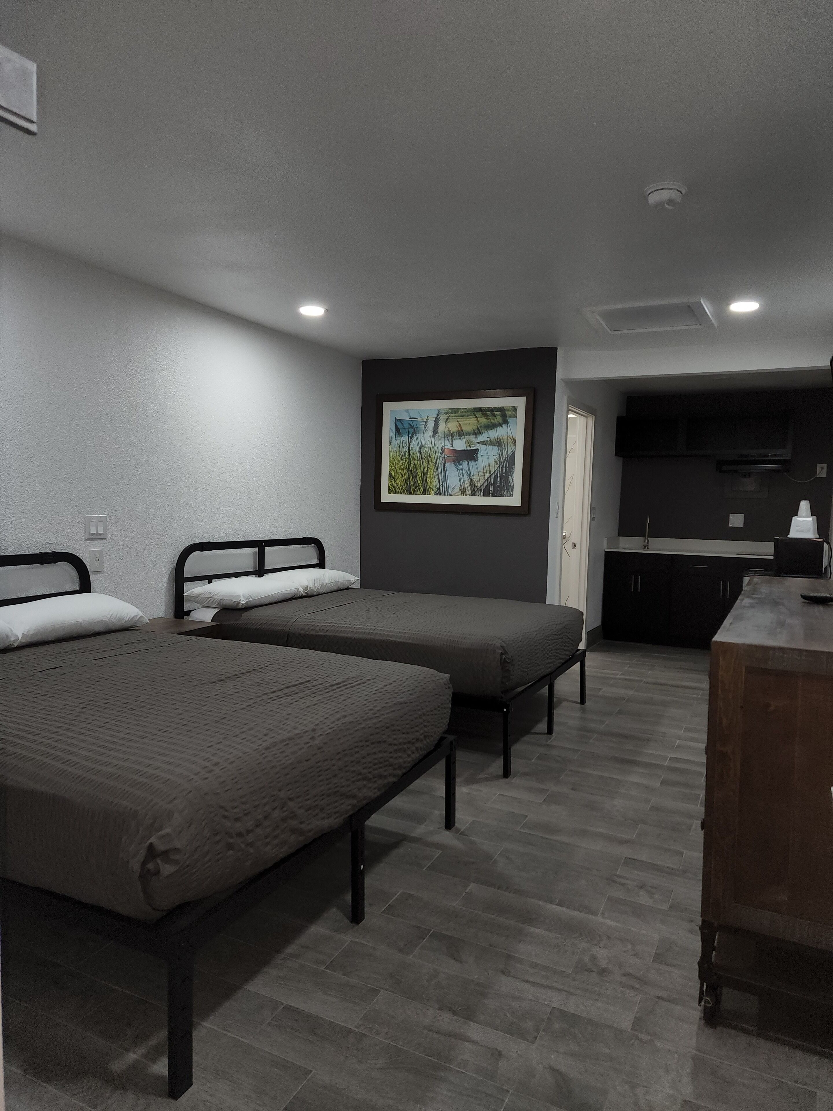 A room with two single beds, a small kitchenette, and a painting on the wall.