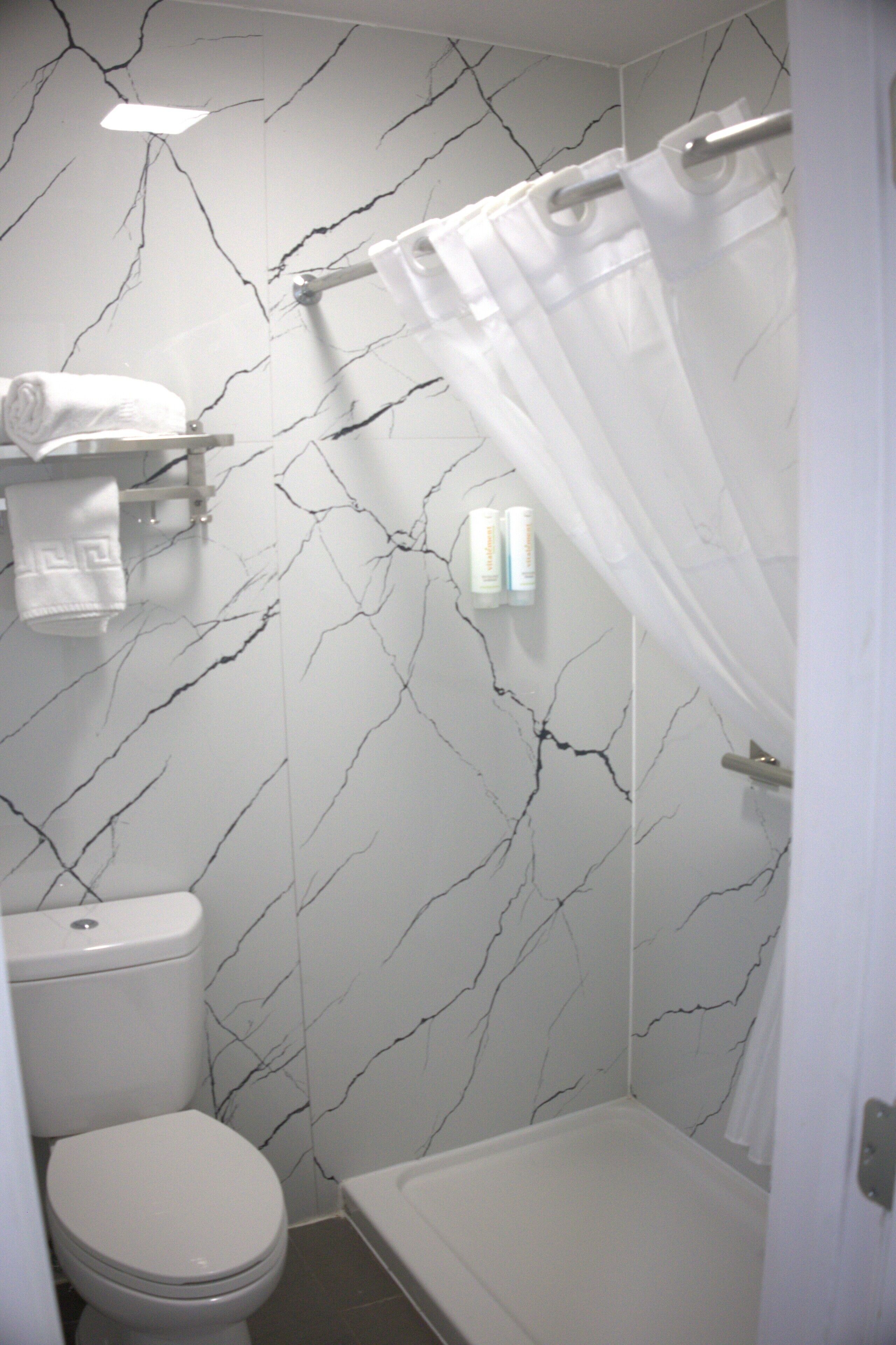 A bathroom with a toilet, a shower with a curtain, and a marble wall.