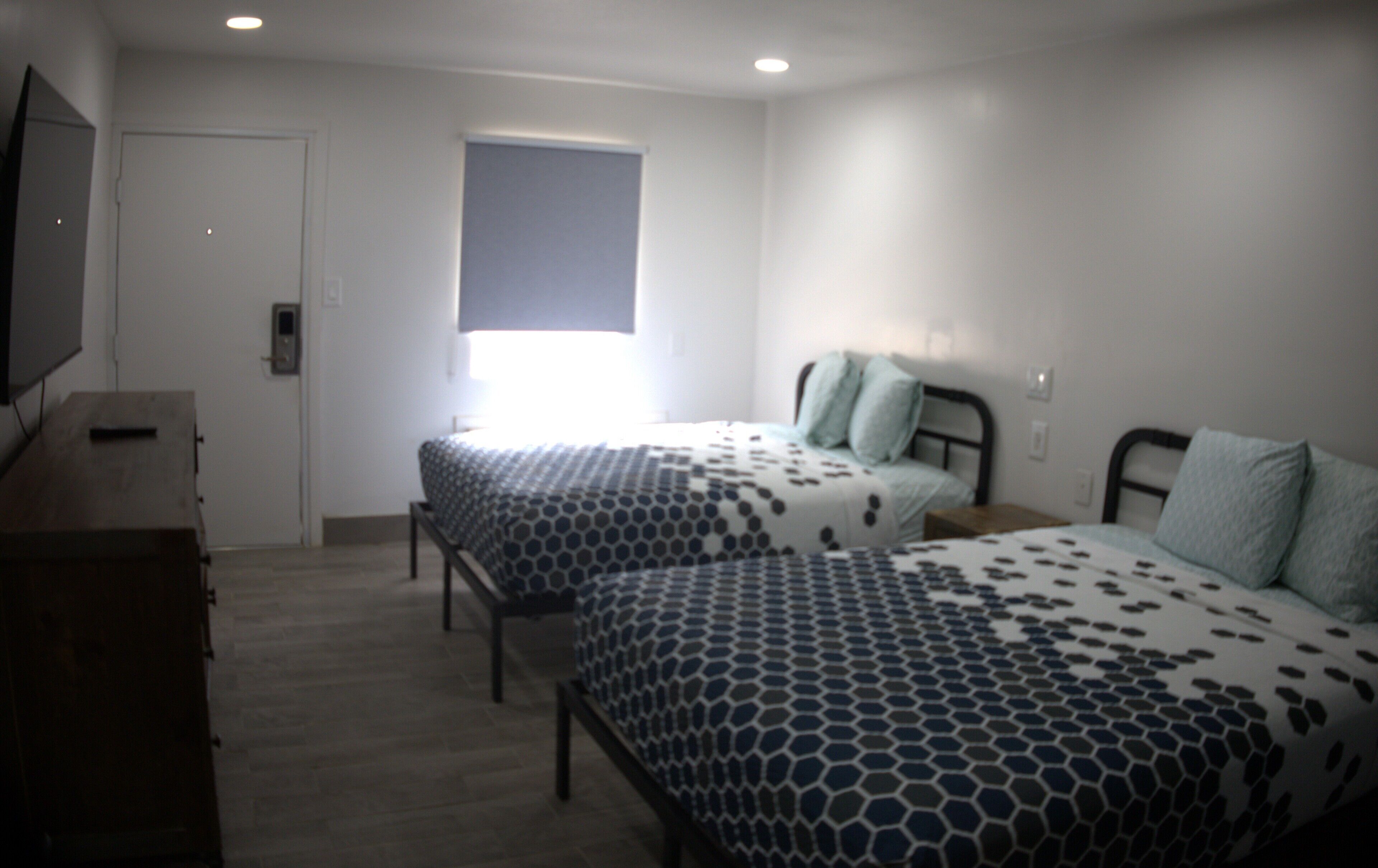 Un dormitorio con dos camas, un tocador, un televisor y una ventana.
