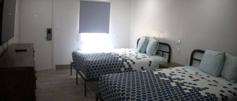 Un dormitorio con dos camas, un tocador, un televisor y una ventana.
