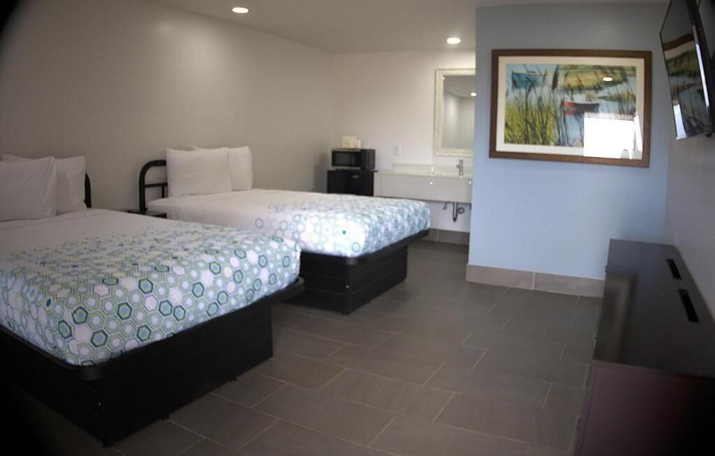 A hotel room with two beds, a small desk, a mirror, and a painting on the wall.