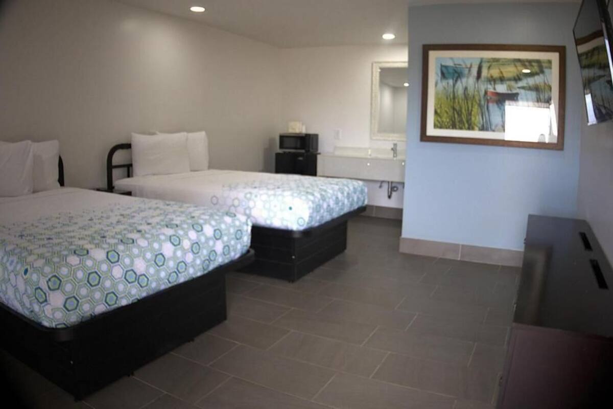 A hotel room with two beds, a small desk, a mirror, and a painting on the wall.