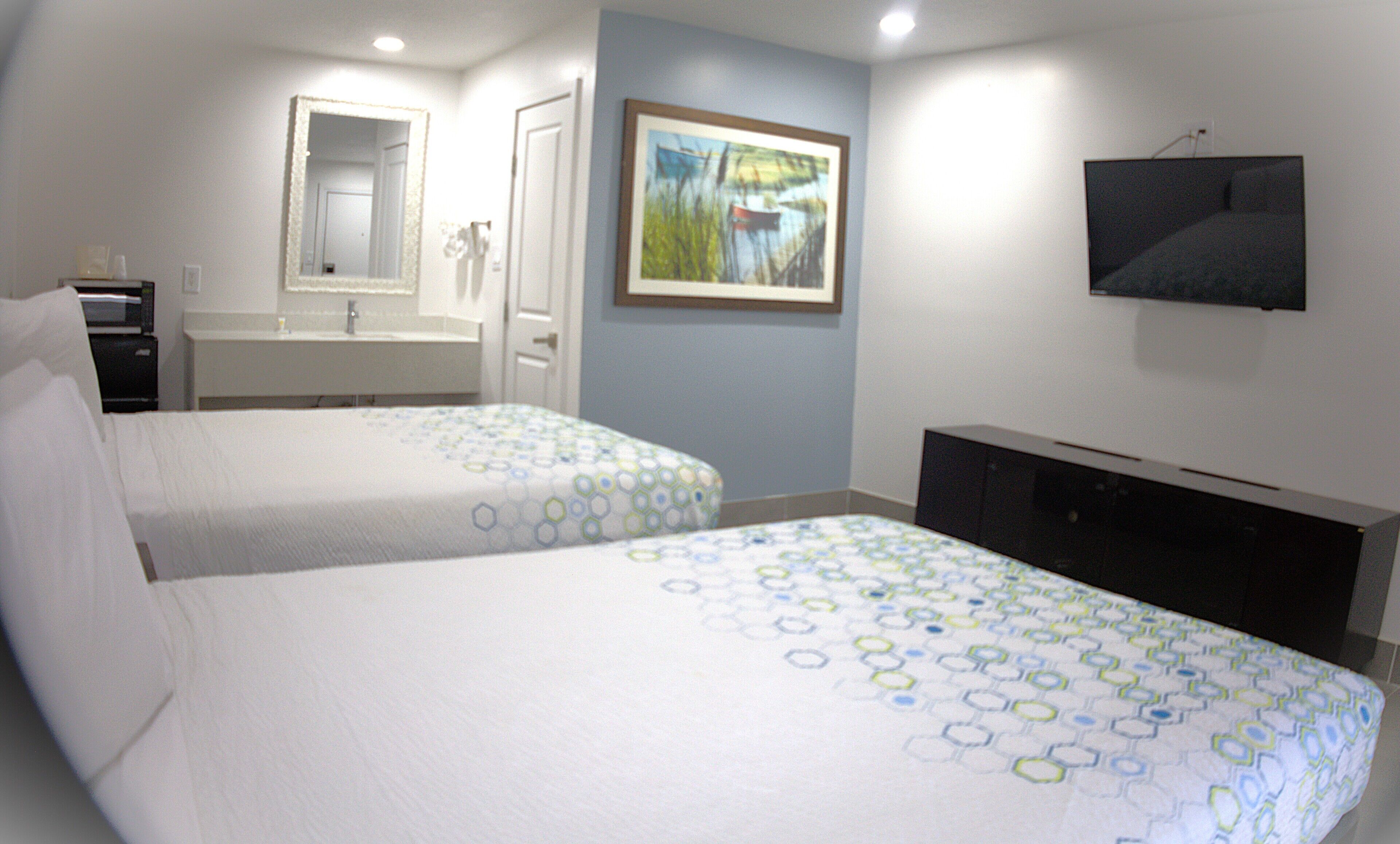 A hotel room with two beds, a bathroom, a TV, and a painting on the wall.