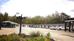 A motel with a parking lot, a covered outdoor seating area, and a landscaped garden with red flowers.